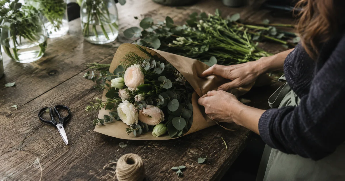 Établi d'une fleuriste avec un bouquet de mariée, une composition de deuil sobre et un bon de livraison prêt à partir