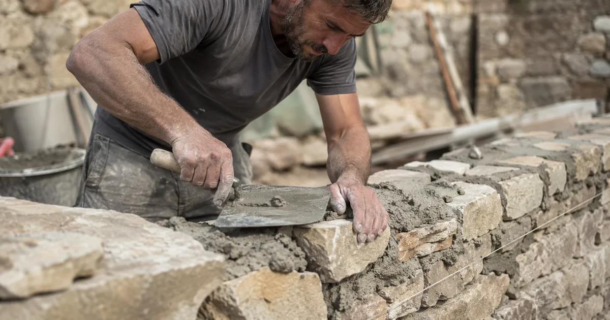 Un maçon consulte le site de son entreprise sur son téléphone devant un mur en parpaings en construction