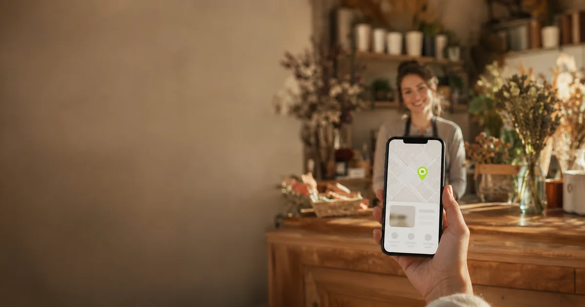 Fleuriste souriante dans sa boutique en Loire-Atlantique et smartphone affichant sa fiche de localisation en ligne